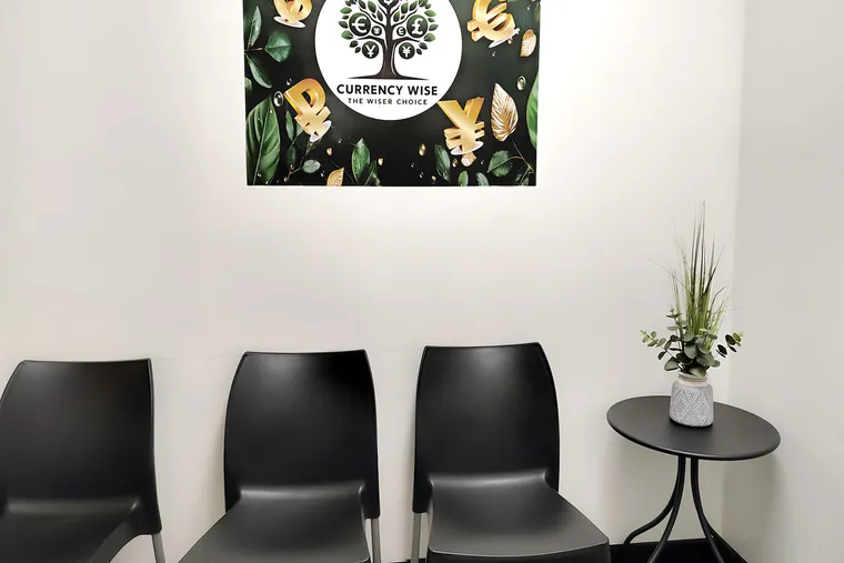The waiting area inside Currency Wise Exchange, with two chairs, a side table and the Currency Wise artwork on the wall.